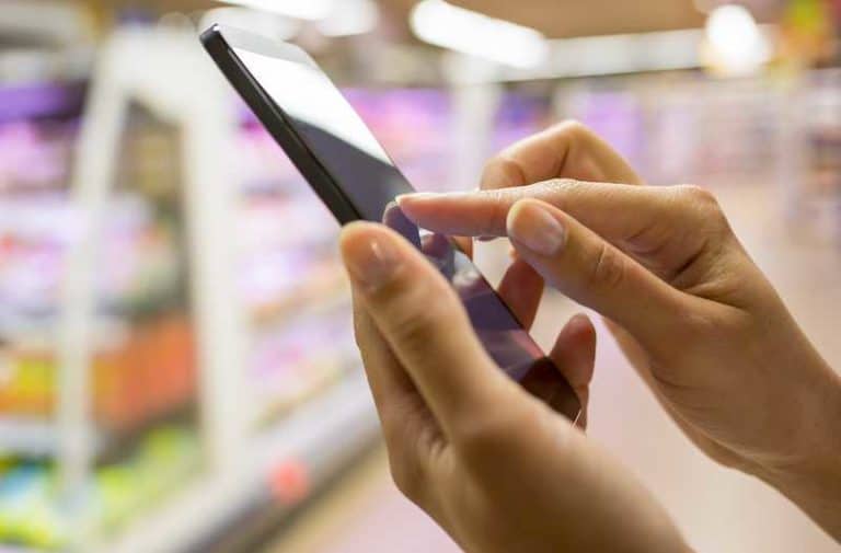 Twee handen bedienen een smartphone met koelschappen in een supermarkt op de achtergrond