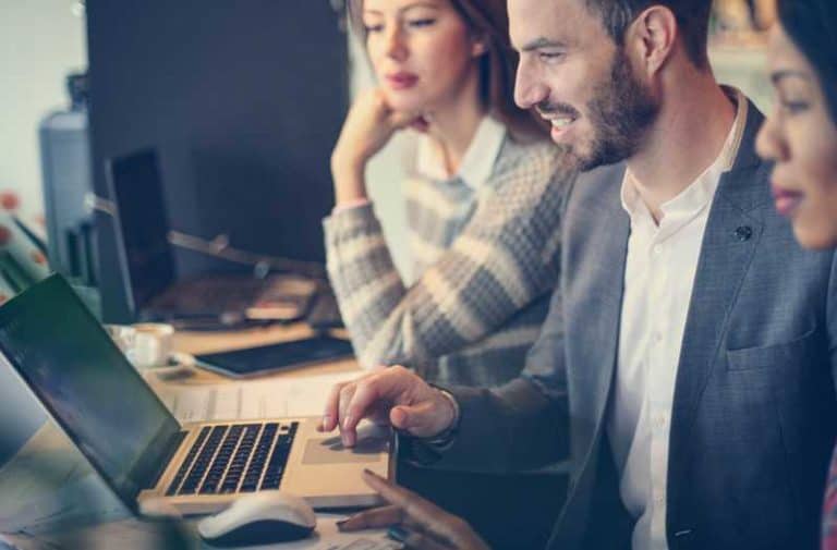 Drie mensen werken samen aan een project aan een bureau met een laptop