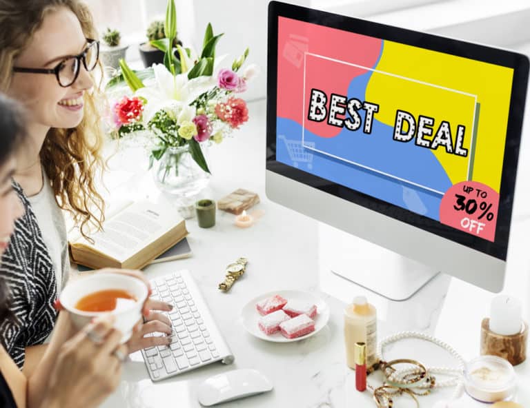 Een vrouw met blond haar en een bril zit voor een computer met een ‘best deal’ afbeelding op het scherm