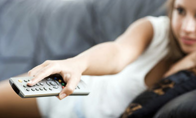 Een vrouw met een witte jurk ligt op de bank en richt haar afstandsbediening naar de televisie