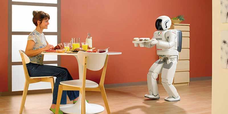 Een vrouw zit aan tafel te ontbijten een wordt door een Asimo-robot bediend