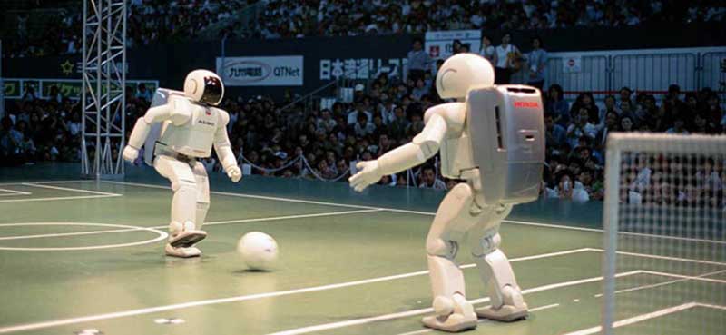 Twee Honda Asimo-robots spelen zaalvoetbal terwijl het publiek toekijkt