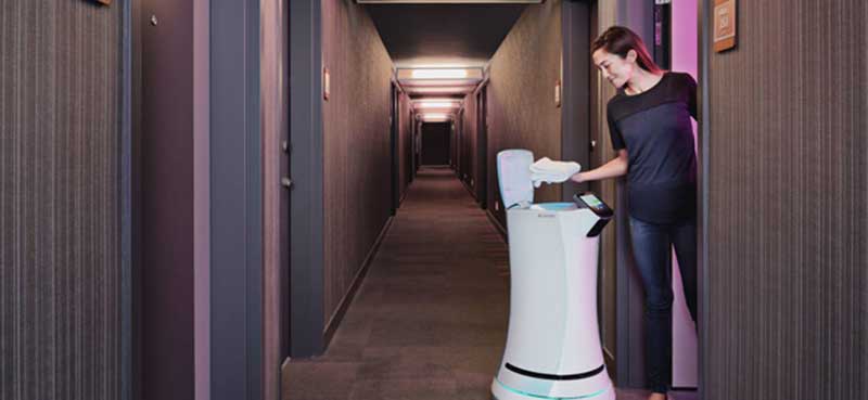 SaviOne roomservicerobot brengt een handdoek naar een vrouw in een hotelkamer