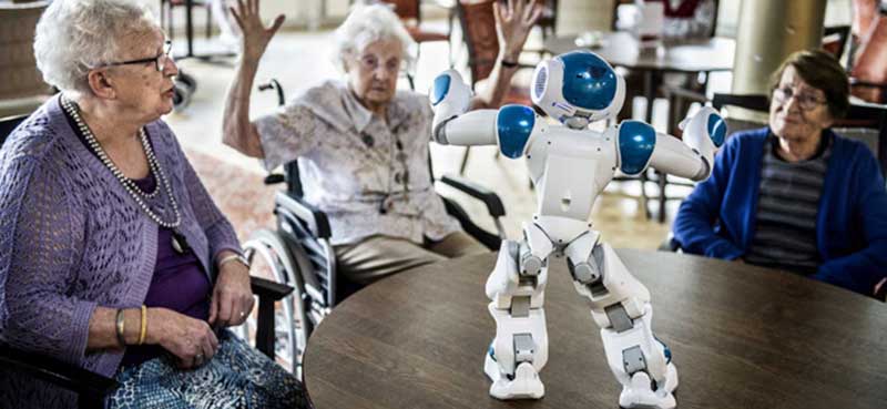 Drie bejaarde vrouwen communiceren met een kleine robot die op een ronde tafel staat