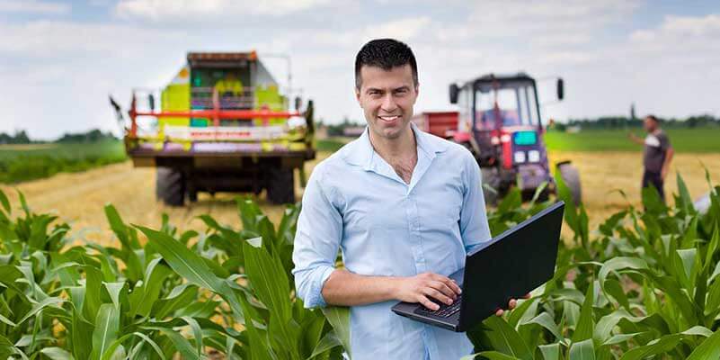 Man in maisveld met laptop en tractors