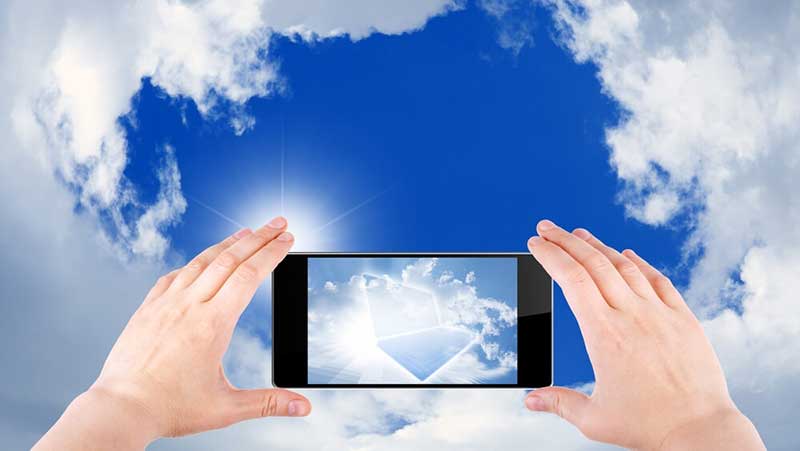 Twee handen houden smartphone vast en maken foto van blauwe lucht met wolken