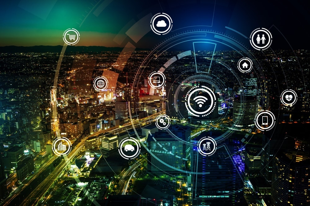 Een digitale representatie van het IoT met verschillende icoontjes zweeft boven een stad in de avond