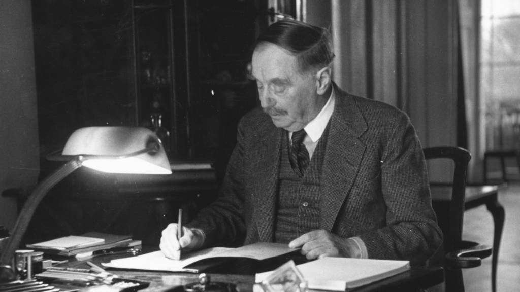 Zwart-wit foto van H.G. Wells die aan zijn bureau zit en schrijft