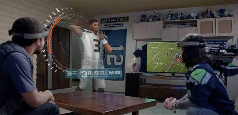 Een man en een vrouw met Microsoft HoloLens headsets kijken naar een virtueel beeld van een speler in hun woonkamer