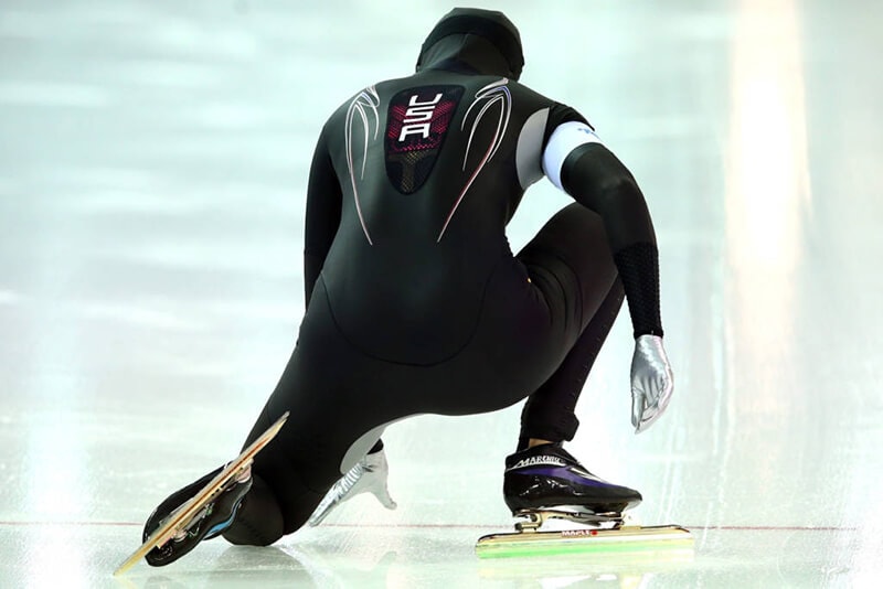 Een snelschaatser in een zwart pak staat in de startpositie