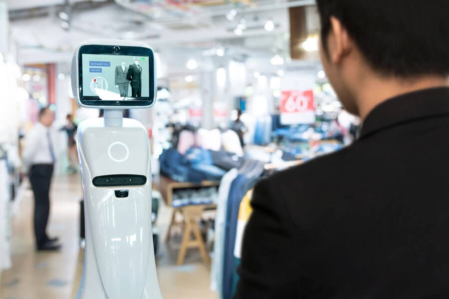 Een man staat in een winkel voor een witte robot uitgerust met een scherm met informatie