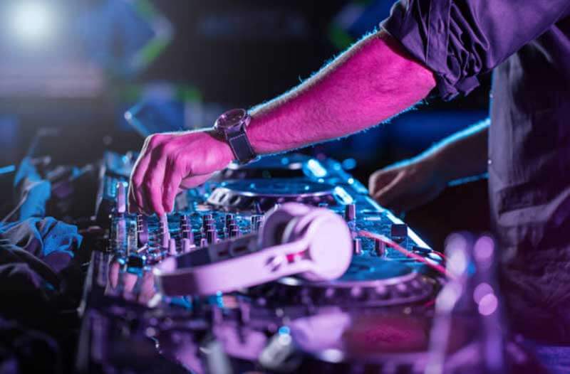 A DJ turning knobs on a soundboard, with blurred white headphones in the foreground