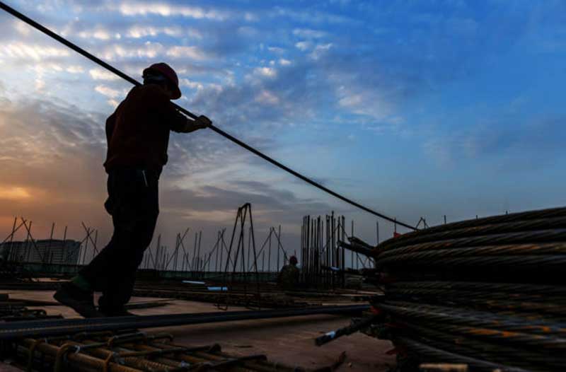 A worker with a protective helmet moving rebar at a construction site at sunset
