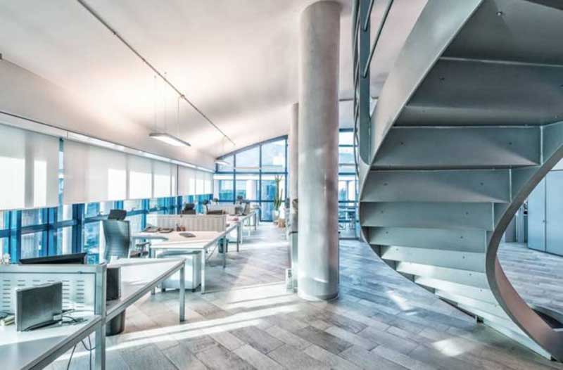 Bright office area with workstations on the left, and a spiral staircase on the right