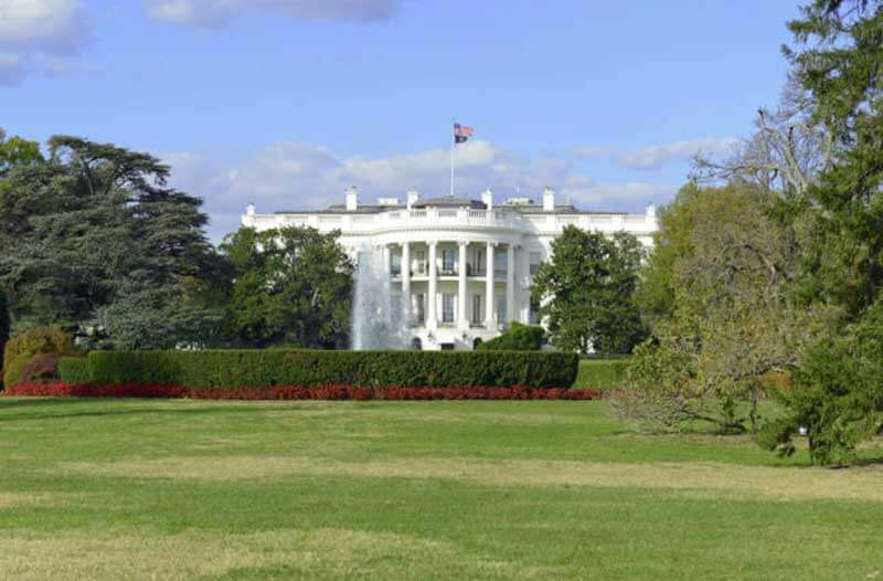 The White House with the US flag atop, and lawn and trees surrounding it