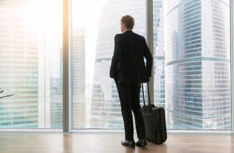 man with a suitcase looking through a window at skyscrapers