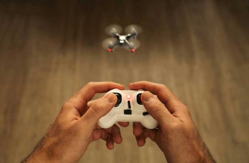 Two hands holding a white controller to fly a mini drone