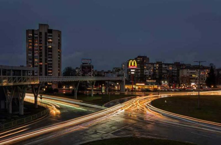 Een een stad bij avond met een groot verlicht verkeersknooppunt met in de verte een verlicht McDonald’s-logoEen een stad bij avond met een groot verlicht verkeersknooppunt met in de verte een verlicht McDonald’s-logo