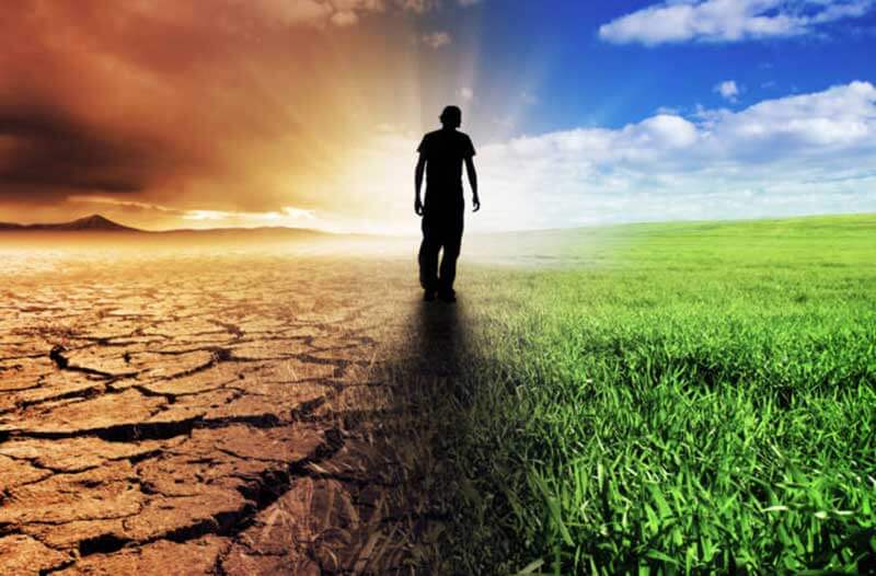 Silhouette of a man walking down a field featuring a dry and deserted landscape on the left and grassland on the right