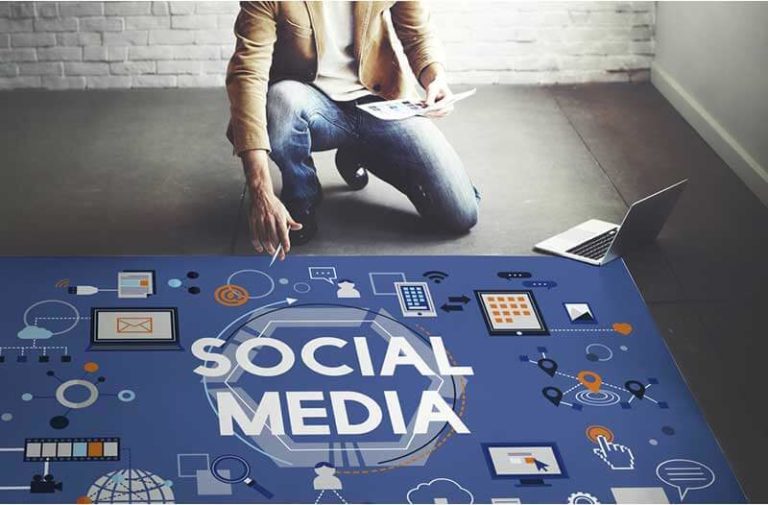 Een man zit geknield op de vloer naast een laptop en een grote afbeelding van een social media-model
