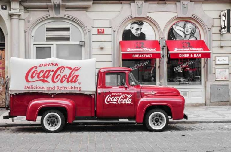 Een ouderwets gebouw met afbeeldingen van filmsterren waar een klassieke rood-witte Coca-Cola vrachtwagen geparkeerd staat