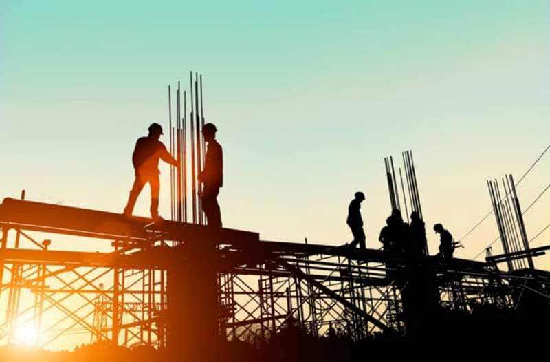 Workers standing on metal scaffolding on a construction site at sunset