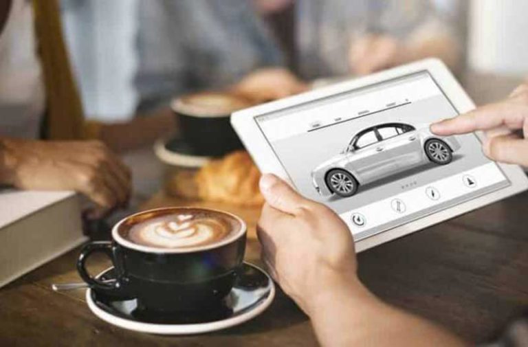 Personen aan een tafel met kopjes koffie en een tablet met een auto op het scherm