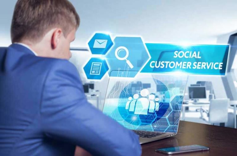 Man in blauw pak zit achter laptop waarboven blauwe iconen zweven over social customer service