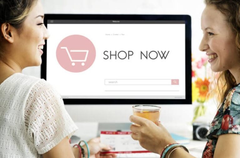 Twee vrouwen zitten achter een computer met de woorden ‘shop now’ op het scherm