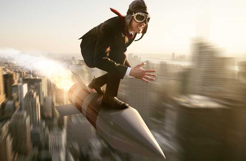 Person with aviator’s hat and goggles on a rocket flying above a city
