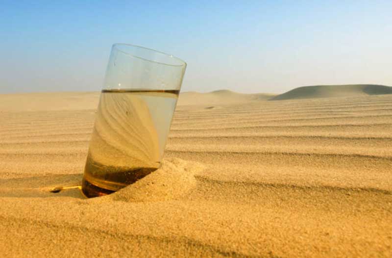Glass of water in desert sand with blue sky