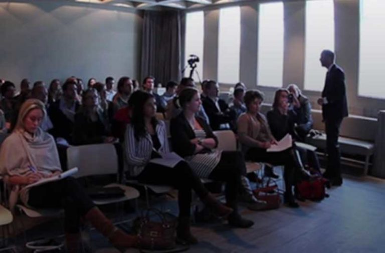 Een zaal vol met mensen op stoelen die een presentatie bijwonen