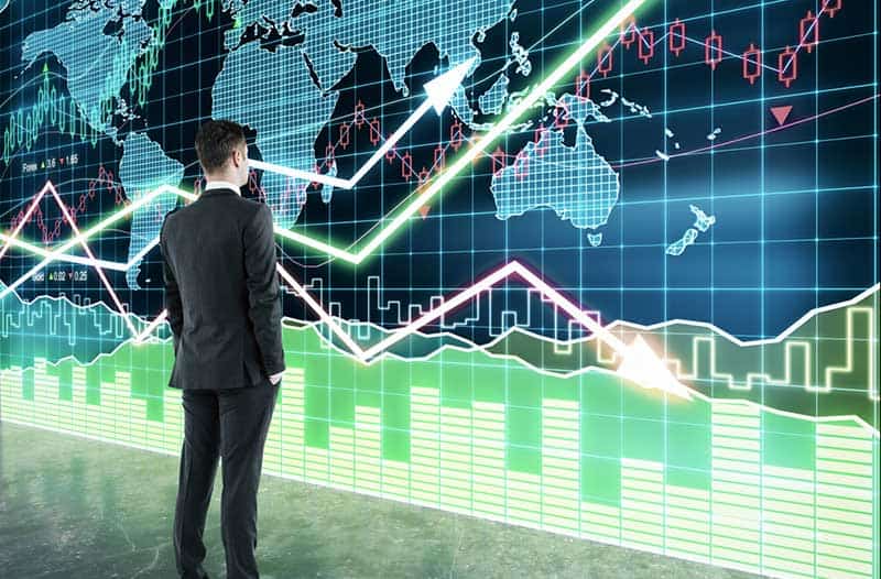 Man in suit standing in front of a huge digital world map with graphs and lines