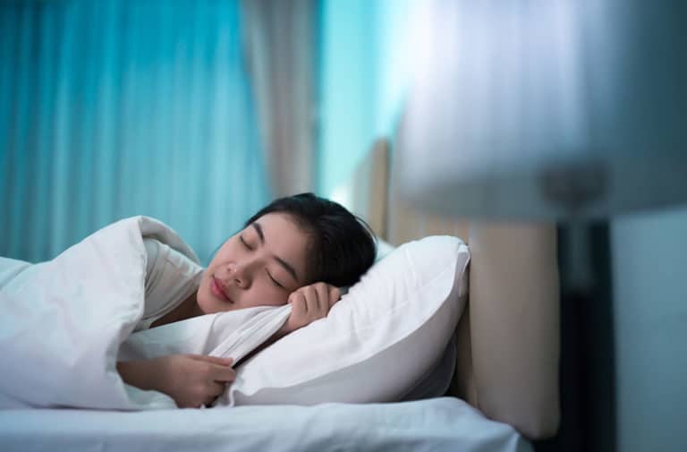 Vrouw met donker haar ligt in een bed met wit beddengoed te slapen