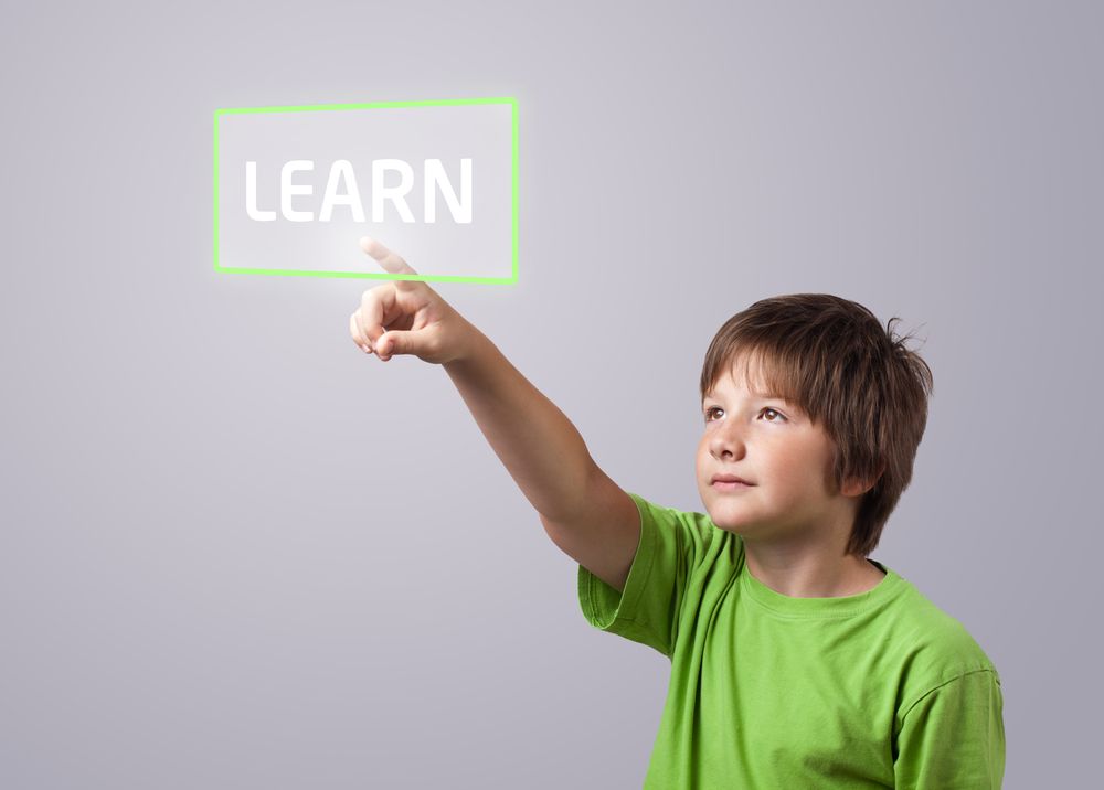 Kind met een groen shirt aan wijst naar het digitale woord ‘learn’ dat voor hem zweeft