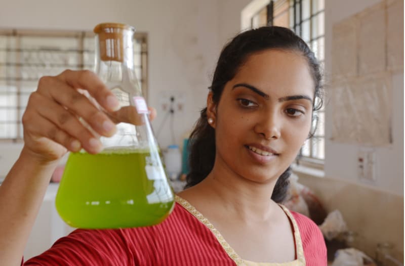 Vrouw houdt een laboratoriumfles met een groene vloeistof omhoog.