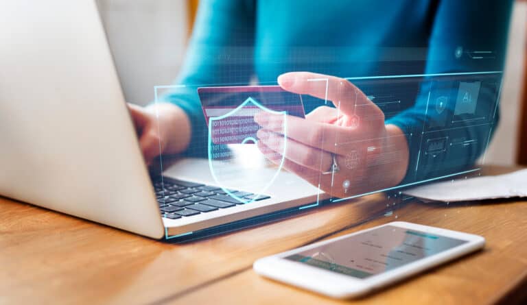 AI-marketing: een persoon met een blauwe trui zit op een witte laptop te typen en houdt een pasje vast terwijl AR-infographics boven het toetsenbord zweven.