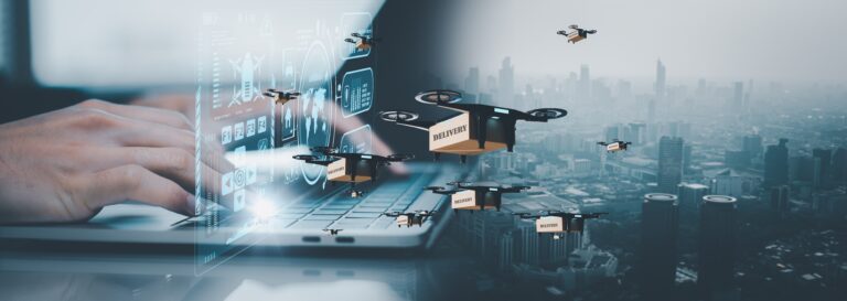 Twee handen die typen op een laptop-keyboard met op de achtergrond een futuristische stad waar drones overheen vliegen: een representatie van de toekomst van logistiek en voorraadbeheer.