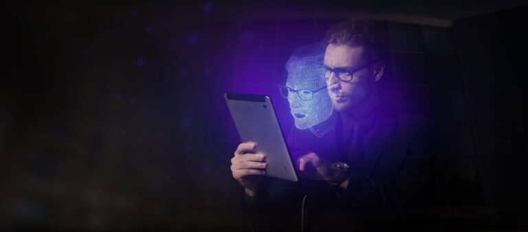 Een man met een bril kijkt naar een tablet en een holografische projectie van een digitaal menselijk gezicht zweeft voor zijn gezicht.