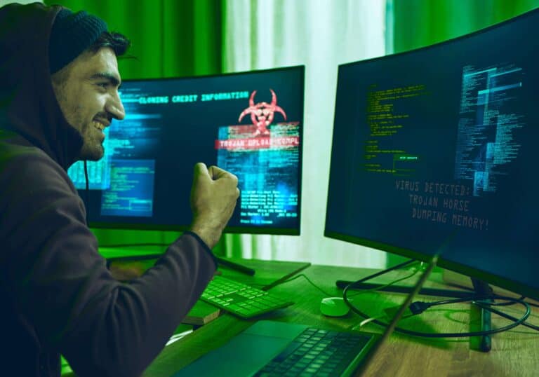 Een hacker heft triomfantelijk zijn vuist voor computerschermen die code en een viruswaarschuwing tonen met de tekst ‘Trojan Horse Dumping Memory’.