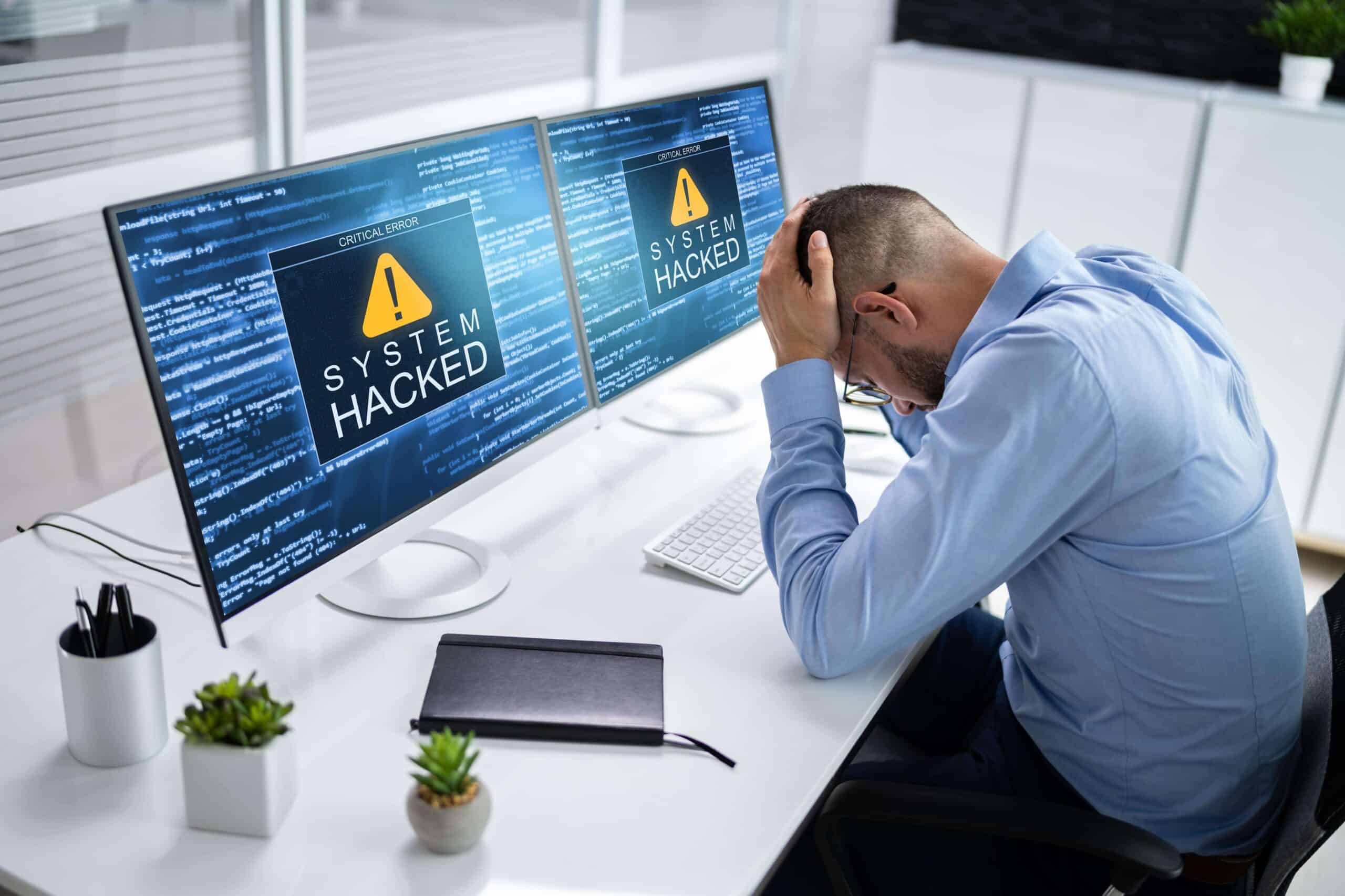 A stressed man in an office discovers his computer system has been hacked.