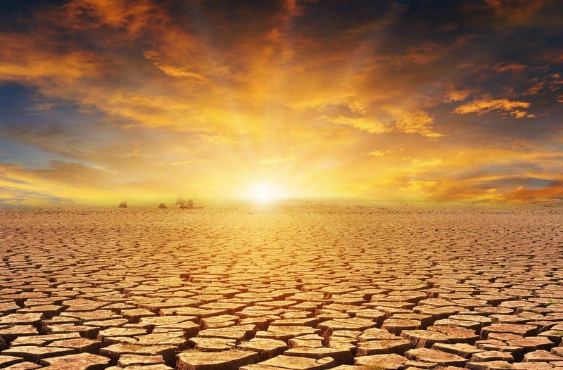 Droge, gebarsten grond met oranje wolken erboven