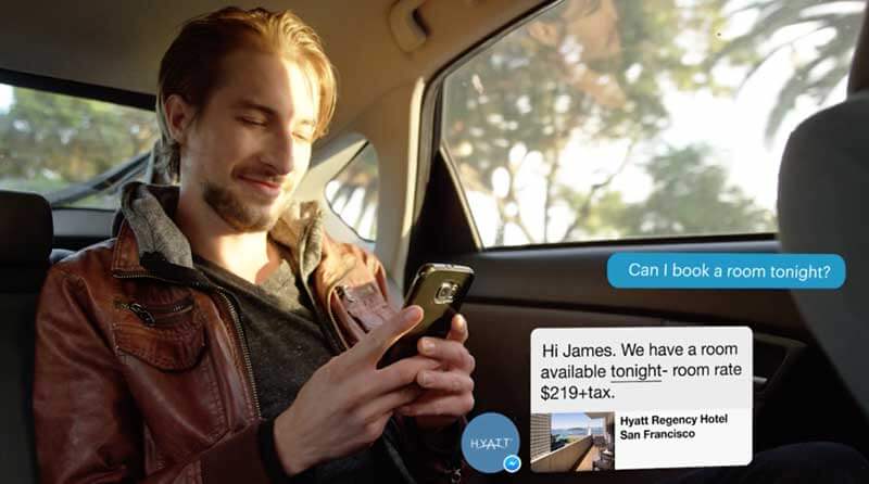  Man sitting in the backseat of a car holding his smartphone and using it to book a room via a chatbot