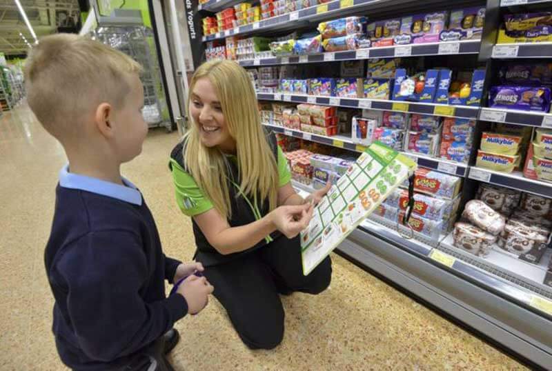 A female grocery store worker smiling at a kid while crouching in front of store shelves