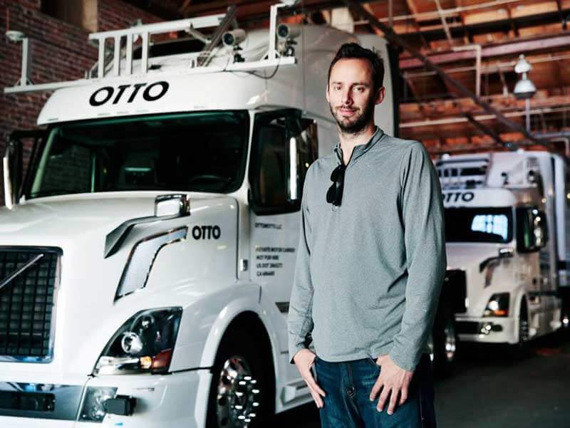  A man standing in front of two Otto’s self-driving trucks