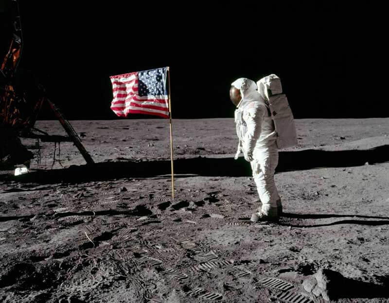 Neil Armstrong standing next to to the US flag on the moon