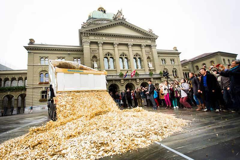 A truck unloading some kind of material in front of an old building with a crowd watching