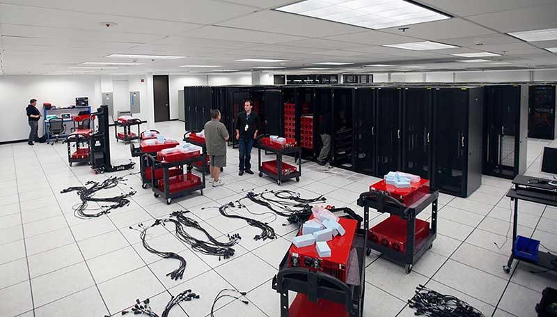 Three men in a large room setting up a data centre with several rows of server hardware boxes behind them