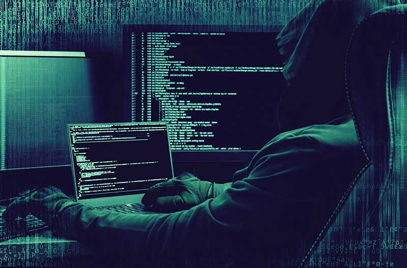 Hacker with hoodie sitting in front of computer screens
