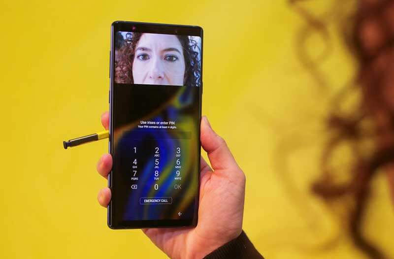 A woman using facial recognition technology on her smartphone, on a yellow background. 